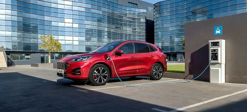 Ford Kuga töltés közben egy üvegépület előtt