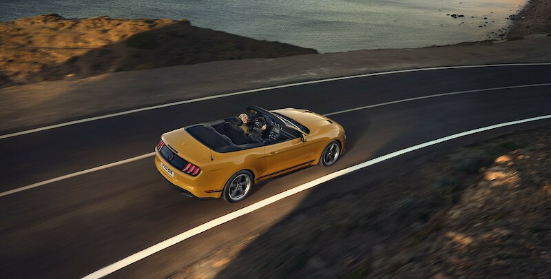 Sárga Ford Mustang halad a szerpentinen a tengerpart mellett