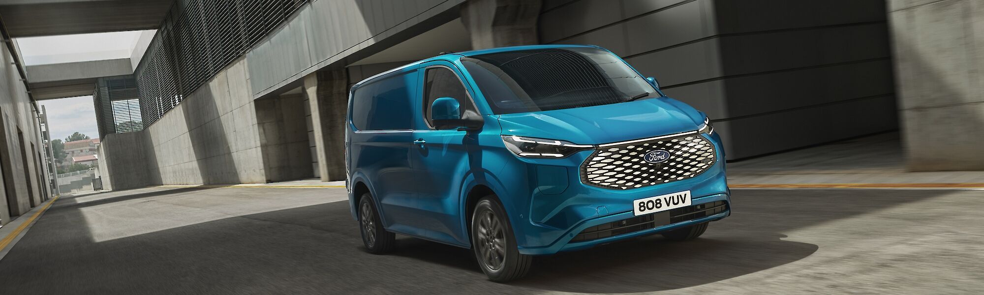 Kék Ford E-Transit Custom halad egy iparterületen